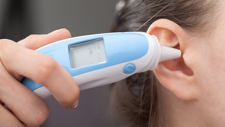 Digital ear thermometer next to a woman's ear.