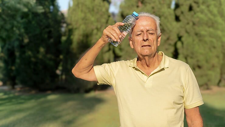 Elderly man holding a water bottle to his forehead